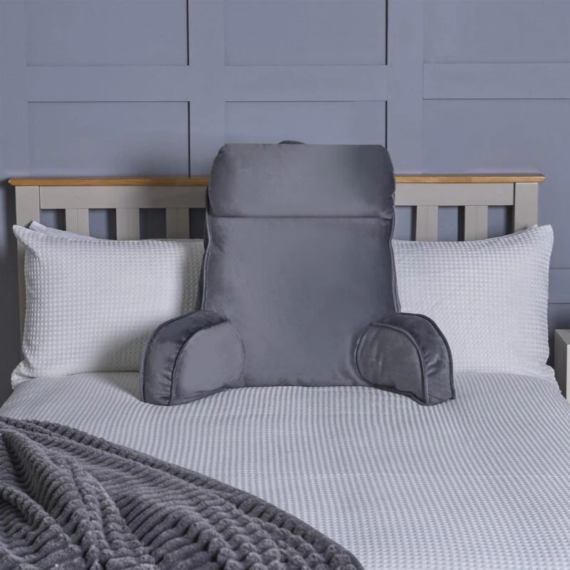 Grey lumbar support pillow on a bed with white pillows and a grey blanket.