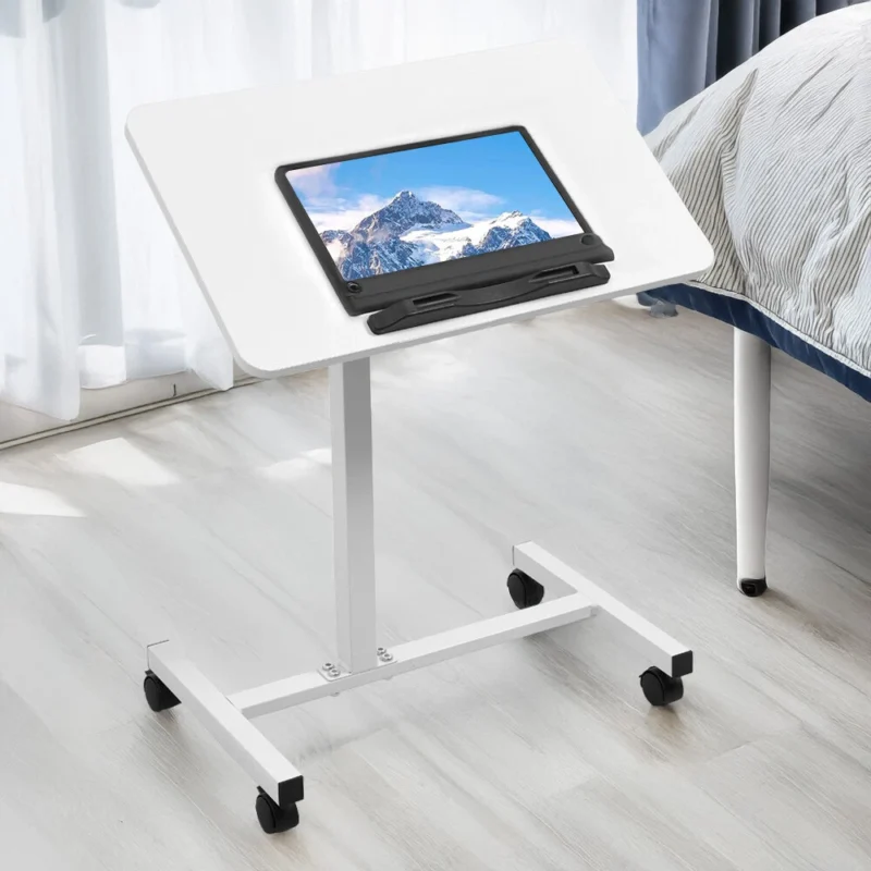 White over bed table tray with a tablet on top, next to a bed.