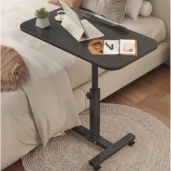 Black over bed table tray with items on it beside a bed.