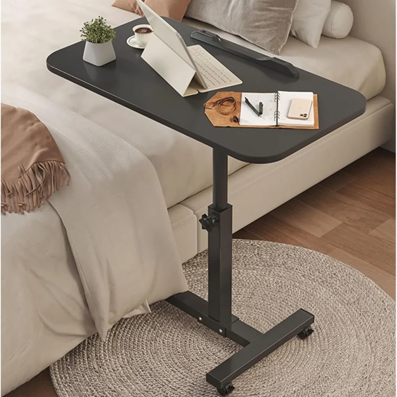 Black over bed table tray with items on it beside a bed.