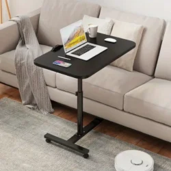 Black over bed table tray with a laptop and mug beside a beige sofa.