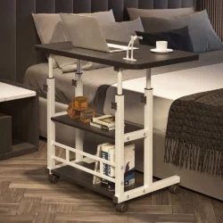 Height adjustable over bed table with a laptop and cup next to a bed.