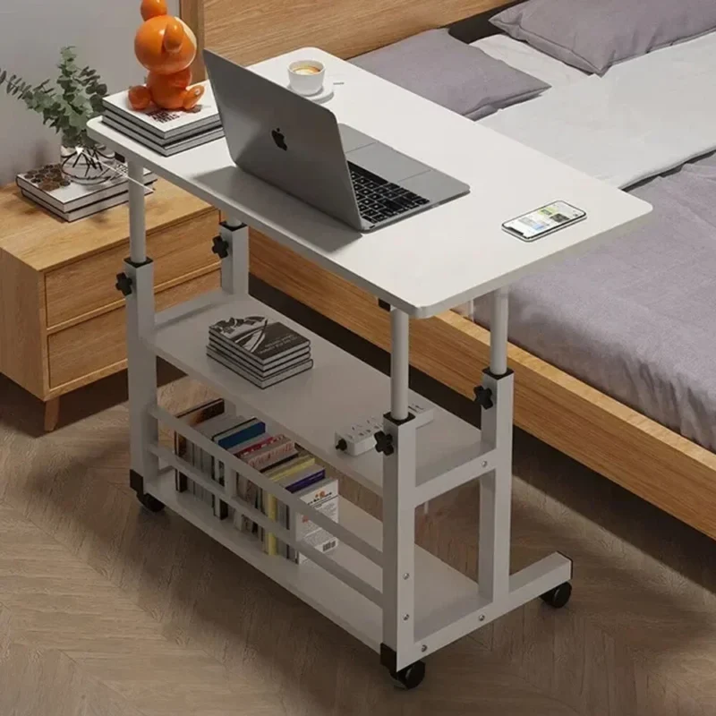 White over bed table with laptop and books, next to a bed.