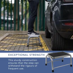 Person standing on a grey step stool next to a car in a parking area.