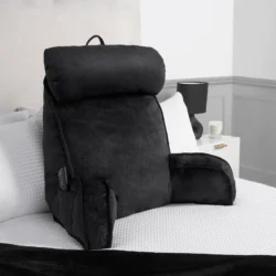 Black lumbar support pillow with headrest and arms on a bed.