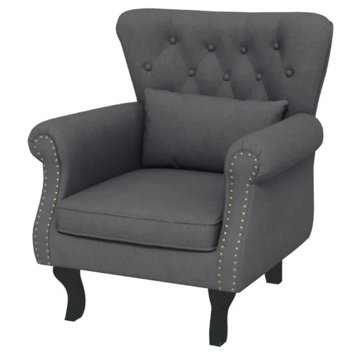 Dark grey tufted wingback armchair with pillow and wooden legs.