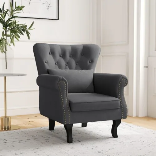 Dark grey tufted wingback armchair with pillow in a room.